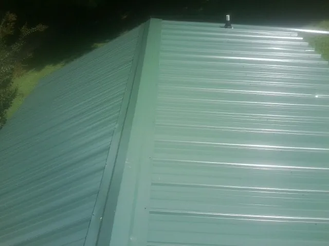 New green metal panels meeting at the ridge of a roof — Flat Roof Repair work by our crew in Montrose